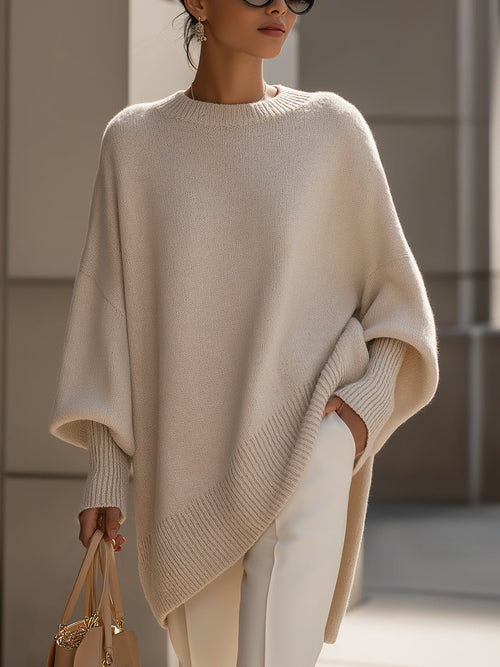 Asymmetrical knit poncho sweater featuring a round neckline, relaxed draped silhouette, ribbed cuffs, and side-point hem