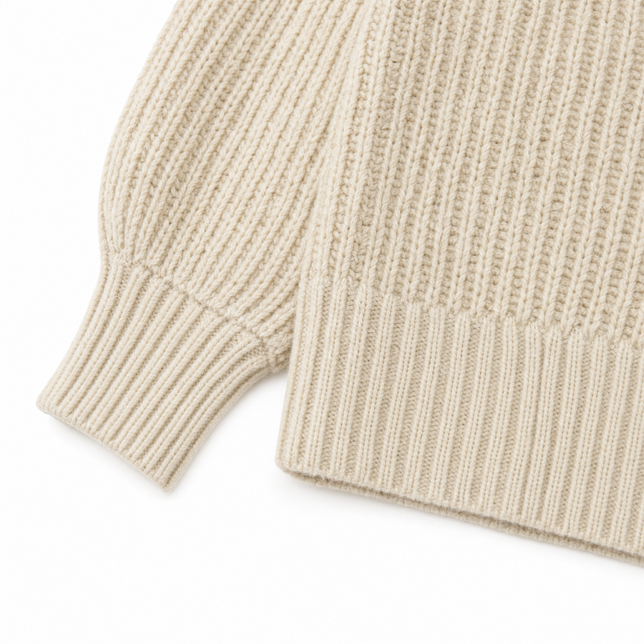 Close-up of a cream-colored ribbed knit sweater showing the sleeve cuff and hem detail against a white background.