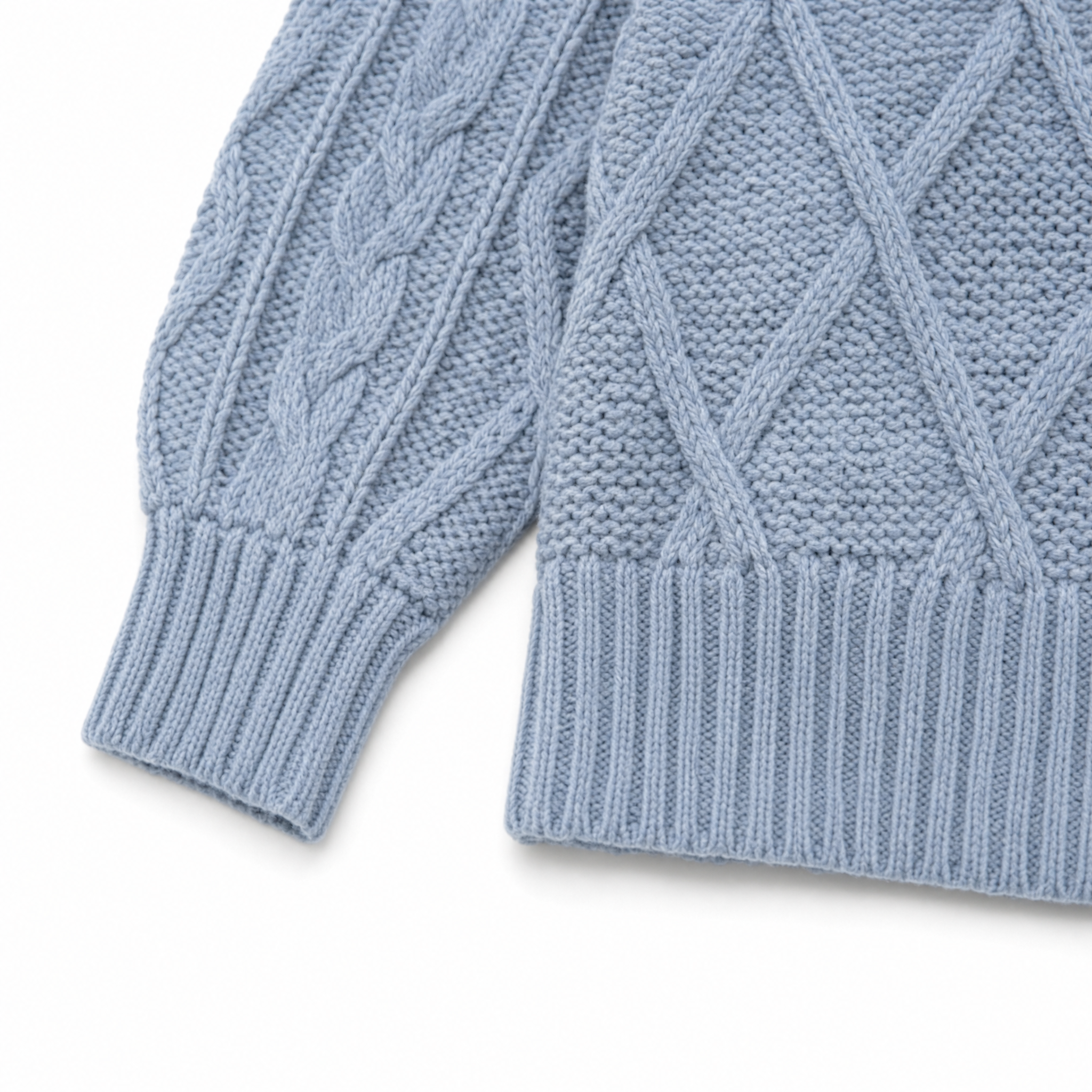Close-up of a light blue cable-knit sweater showing the ribbed cuffs and textured knit patterns on a white background.