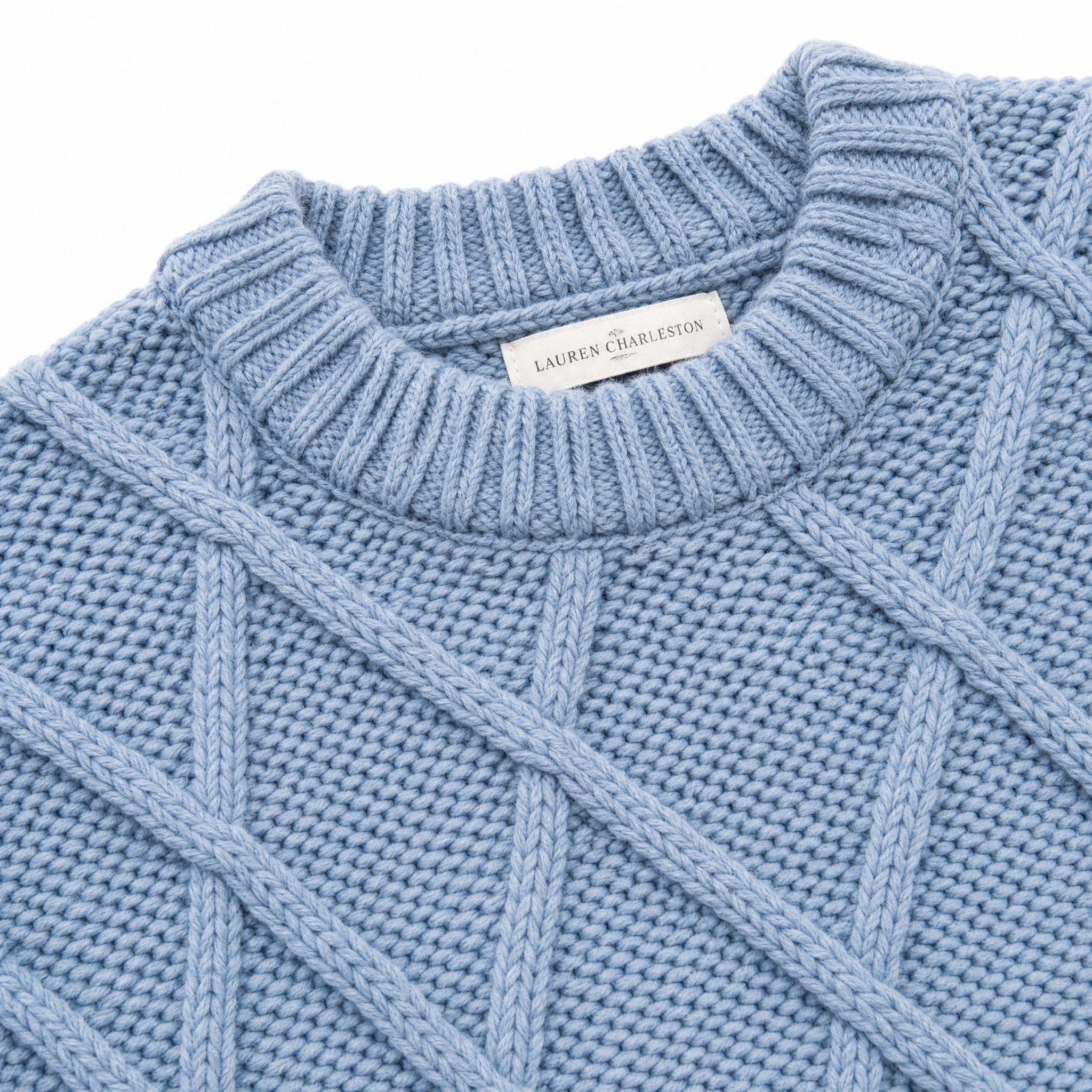 Close-up of a light blue ribbed knit sweater with a visible Lauren Charleston neck label, showing the textured cable-knit pattern and collar detail on a white background.